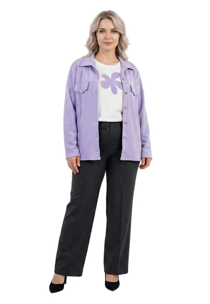 Ολόσωμη λήψη από επίσημο σετ για μεγάλα μεγέθη, με απαλό μωβ σακάκι και λευκή μπλούζα διακοσμημένη με λουλούδι.