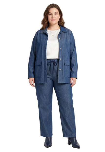 Ολόσωμη λήψη plus size μοντέλου που φοράει μπλε σετ με τζιν σακάκι και παντελόνι, συνδυασμένο με λευκό τοπ, σε λευκό φόντο.