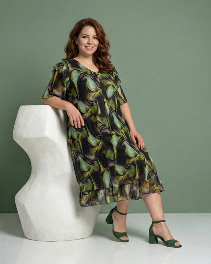 Επίσημο σιφόν φόρεμα plus size με πολύχρωμο μοτίβο και αέρινη γραμμή, με λεπτομέρειες βολάν στο τελείωμα, σε ολόσωμη λήψη με το μοντέλο καθιστό.