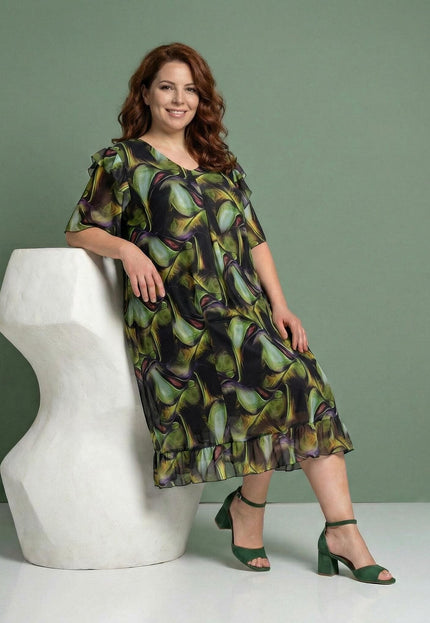 Επίσημο σιφόν φόρεμα plus size με πολύχρωμο μοτίβο και αέρινη γραμμή, με λεπτομέρειες βολάν στο τελείωμα, σε ολόσωμη λήψη με το μοντέλο καθιστό.