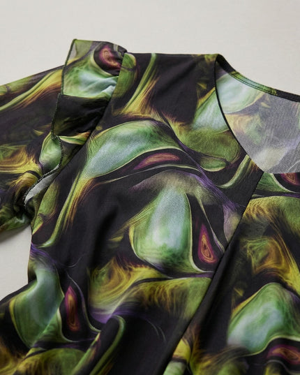 Κοντινή λεπτομέρεια από επίσημο σιφόν φόρεμα plus size με πολύχρωμο μοτίβο. Διακρίνονται οι πράσινες αποχρώσεις, η λαιμόκοψη και το βολάν στον ώμο.