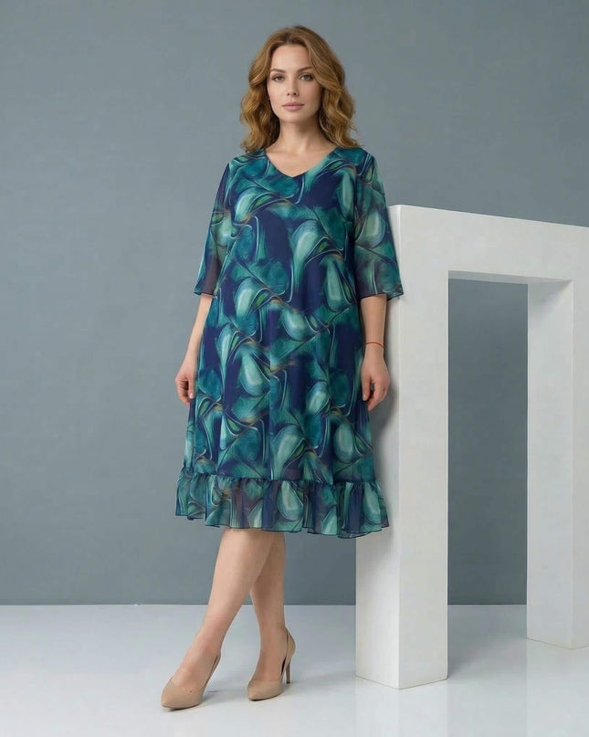 Ολόσωμη λήψη γυναίκας που φοράει επίσημο σιφόν φόρεμα σε μεγάλα μεγέθη, με ντεγκραντέ μπλε σχέδιο, V-ντεκολτέ και βολάν στο τελείωμα.