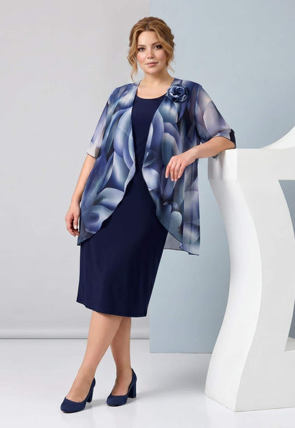 Ολόσωμη λήψη: Σκούρο μπλε επίσημο φόρεμα plus size σε ίσια γραμμή, συνδυασμένο με εντυπωσιακή αέρινη κάπα από σιφόν με μπλε φλοράλ μοτίβο.