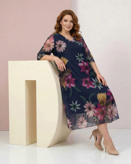 Ολόσωμη λήψη: σκούρο μπλε επίσημο φόρεμα σε μεγάλα μεγέθη, με πολύχρωμο φλοράλ σιφόν, ημιδιάφανα μανίκια και V λαιμόκοψη.