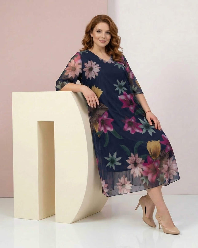 Ολόσωμη λήψη: σκούρο μπλε επίσημο φόρεμα σε μεγάλα μεγέθη, με πολύχρωμο φλοράλ σιφόν, ημιδιάφανα μανίκια και V λαιμόκοψη.