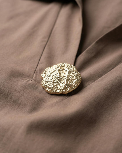 Κοντινή λεπτομέρεια του χρυσού διακοσμητικού στοιχείου στο ντεκολτέ από το επίσημο βαμβακερό πουκάμισο μόκα, σε άνετη γραμμή για plus size σωματότυπους.