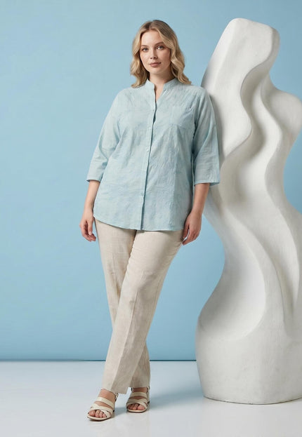 Ολόσωμη λήψη: Plus size επίσημο βαμβακερό πουκάμισο σε ανοιχτό πράσινο χρώμα με διακριτικό φλοράλ κέντημα, φορεμένο με μπεζ παντελόνι.