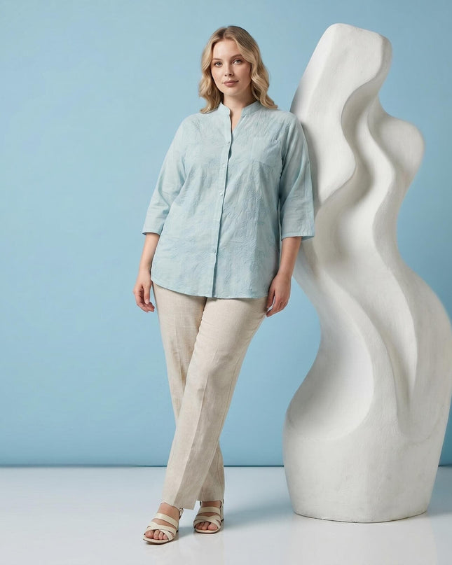 Ολόσωμη λήψη: Plus size επίσημο βαμβακερό πουκάμισο σε ανοιχτό πράσινο χρώμα με διακριτικό φλοράλ κέντημα, φορεμένο με μπεζ παντελόνι.