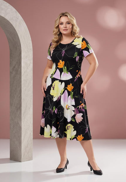 Ολόσωμη λήψη με μοντέλο plus size που φοράει ένα φλοράλ μίντι φόρεμα σε μαύρο χρώμα με εντυπωσιακά πολύχρωμα λουλούδια.