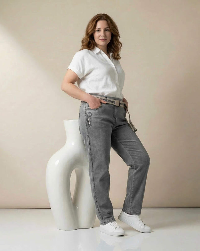Γκρι καθημερινό τζιν παντελόνι σε μεγάλα μεγέθη. Ολόσωμη λήψη όπου το μοντέλο στηρίζεται σε λευκό βάζο, αναδεικνύοντας την ίσια γραμμή και τη ζώνη.