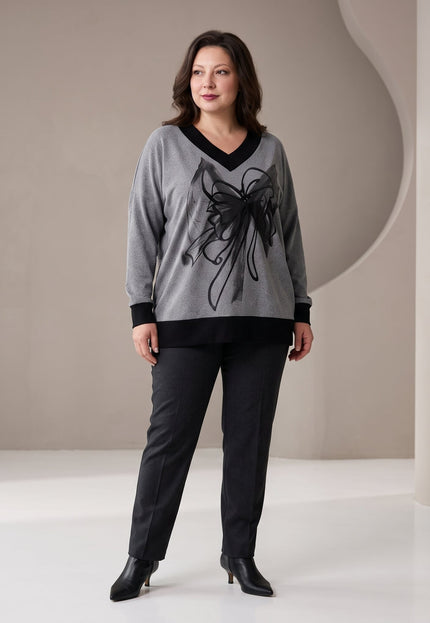 Γυναίκα φορά γκρι τουνίκ με μαύρη V λαιμόκοψη, μαύρο φλοράλ σχέδιο μπροστά και μαύρες λεπτομέρειες στα μανίκια και στο τελείωμα.