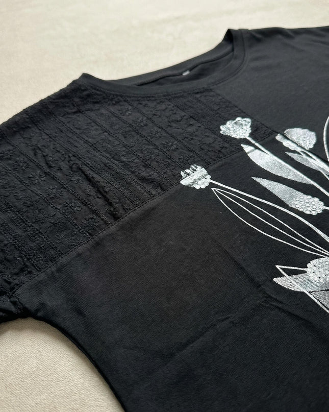 Κοντινή λεπτομέρεια από γυναικεία μαύρη τουνίκ plus size, που δείχνει το σχέδιο με λουλούδια και το ασύμμετρο στοιχείο δαντέλας στον ώμο.