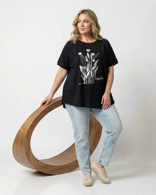 Ολόσωμη λήψη μοντέλου με γυναικεία μαύρη τουνίκ σε μεγάλα μεγέθη. Ξεχωρίζει το λευκό φλοράλ σχέδιο στο μπροστινό μέρος και τα κοντά μανίκια.