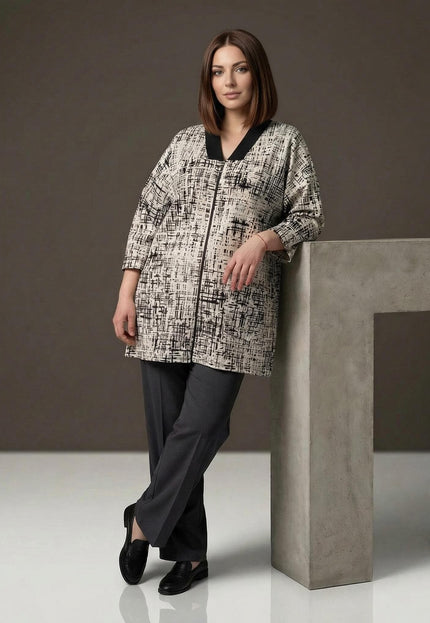Γυναικεία plus size ζακέτα σε μπεζ χρώμα με μαύρο αφηρημένο σχέδιο και V γιακά. Ολόσωμη λήψη σε στούντιο, συνδυασμένη με μαύρο παντελόνι.
