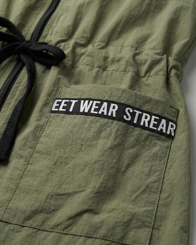 Κοντινή λεπτομέρεια από γυναικείο αντιανεμικό χακί σε μεγάλα μεγέθη, που εστιάζει στο μαύρο κορδόνι στη μέση και την τσέπη με τη διακοσμητική ταινία.