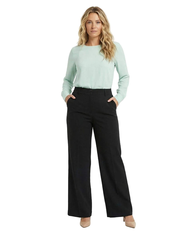 Ολόσωμη λήψη: Γυναικείο επίσημο μαύρο παντελόνι σε ίσια γραμμή για plus size σιλουέτες. Το μοντέλο ποζάρει με τα χέρια στις πλαϊνές τσέπες.