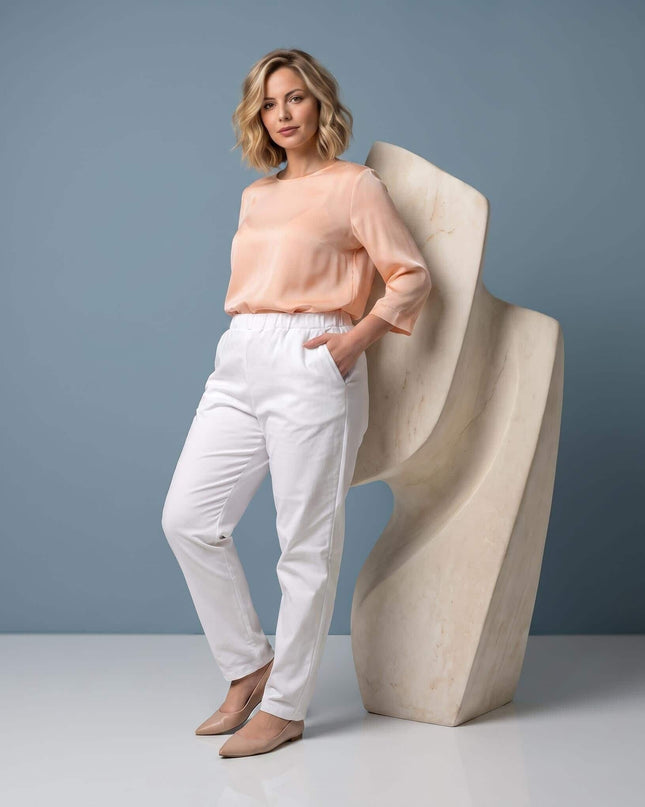 Ολόσωμη λήψη με γυναικείο λευκό παντελόνι plus size σε ίσια γραμμή. Το μοντέλο έχει το χέρι στην μπροστινή τσέπη και φοράει ροδακινί μπλούζα.