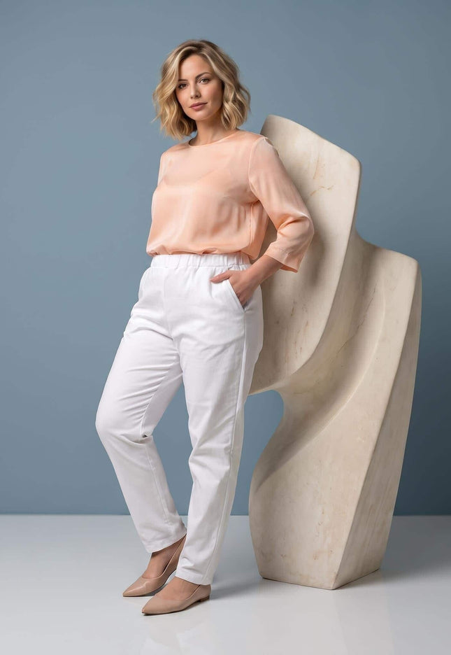 Ολόσωμη λήψη με γυναικείο λευκό παντελόνι plus size σε ίσια γραμμή. Το μοντέλο έχει το χέρι στην μπροστινή τσέπη και φοράει ροδακινί μπλούζα.