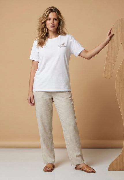 Ολόσωμη λήψη, γυναικείο λευκό βαμβακερό T-shirt σε μεγάλα μεγέθη, με κοντό μανίκι, στρογγυλή λαιμόκοψη και διακριτικό τύπωμα, φορεμένο με μπεζ παντελόνι.