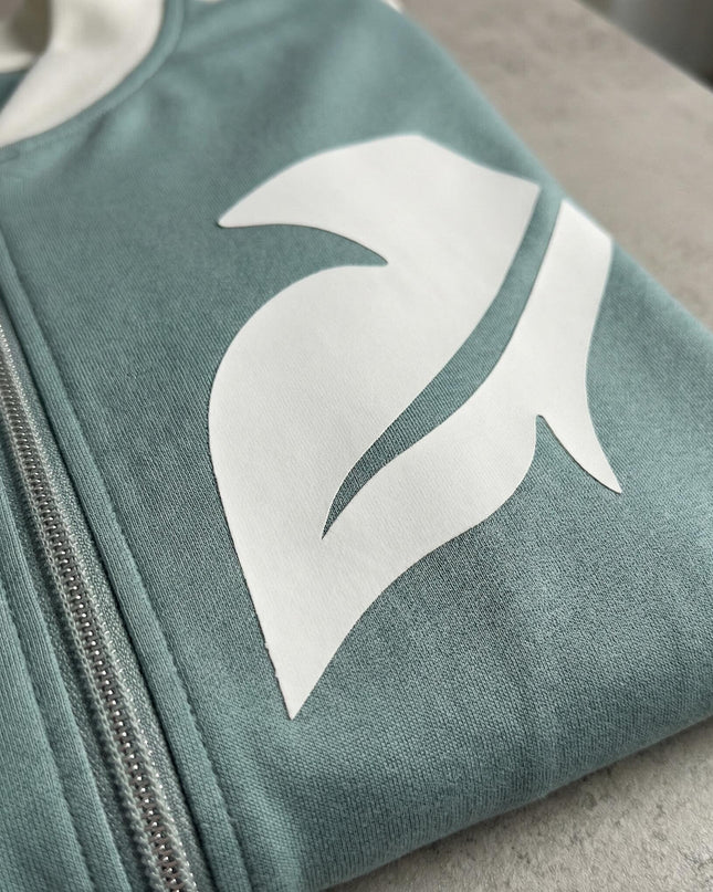 Κοντινή λεπτομέρεια από γυναικείο plus size σετ σε ανοιχτό πράσινο, που εστιάζει στο φερμουάρ και το λευκό σχέδιο από οικολογικό δέρμα στο στήθος.