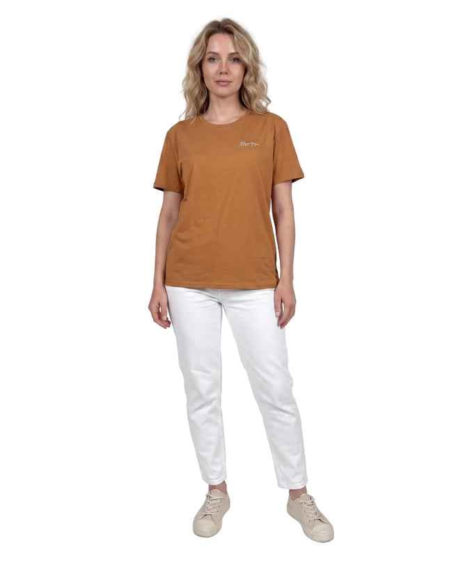 Γυναικείο βαμβακερό t-shirt μεγάλα μεγέθη σε ανοιχτό καφέ χρώμα. Ολόσωμη λήψη του ρούχου φορεμένου με λευκό παντελόνι, που αναδεικνύει την άνετη εφαρμογή.
