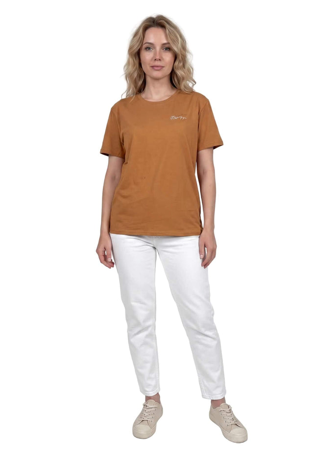 Γυναικείο βαμβακερό t-shirt μεγάλα μεγέθη σε ανοιχτό καφέ χρώμα. Ολόσωμη λήψη του ρούχου φορεμένου με λευκό παντελόνι, που αναδεικνύει την άνετη εφαρμογή.