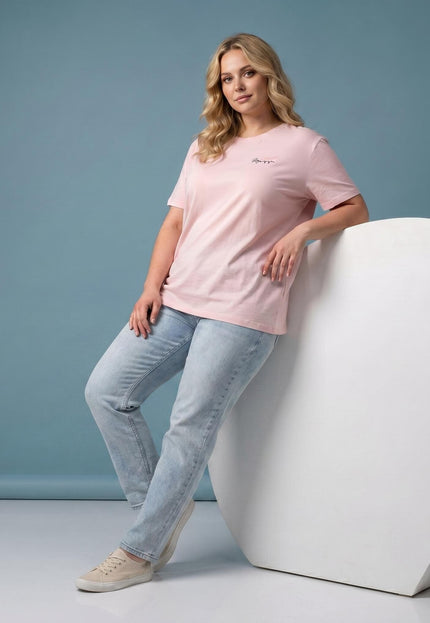 Ολόσωμη λήψη: Γυναικείο t-shirt μεγάλα μεγέθη σε απαλό ροζ χρώμα με κοντά μανίκια και μικρή επιγραφή στο στήθος, συνδυασμένο με τζιν παντελόνι.