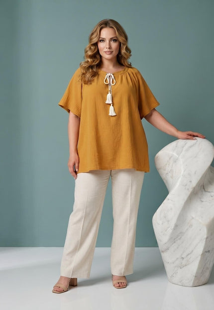 Ολόσωμη λήψη: Καθημερινή γυναικεία τουνίκ plus size σε κίτρινο της μουστάρδας, με άνετη εφαρμογή και διακριτικά κορδόνια με φούντες στο ντεκολτέ.