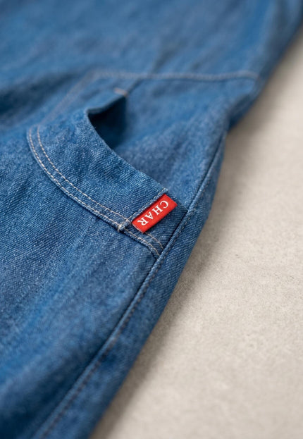 Κοντινή λεπτομέρεια από το καθημερινό denim φόρεμα σε μεγάλα μεγέθη, εστιάζοντας στην μπροστινή τσέπη με τις ραφές και την κόκκινη ετικέτα.