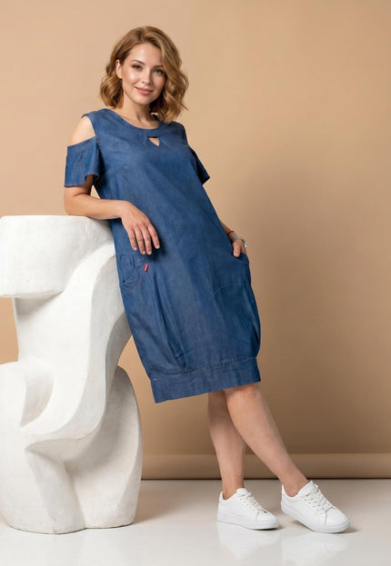 Ολόσωμη λήψη με γυναικείο καθημερινό denim φόρεμα σε μπλε χρώμα, με ανοιχτούς ώμους και πρακτικές τσέπες, ιδανικό για μεγάλα μεγέθη.
