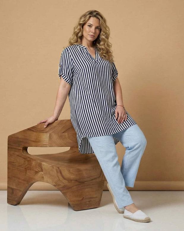 Γυναίκα φοράει ριγέ τουνίκα και λευκό παντελόνι σε στούντιο παρουσιάζοντας καθημερινό ντύσιμο για μεγάλα μεγέθη