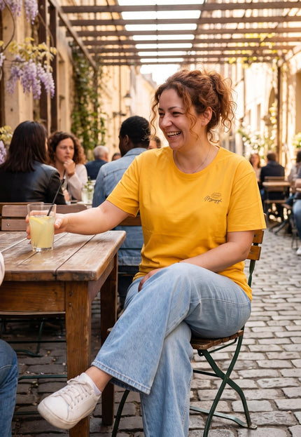 Γυναικείο κίτρινο t-shirt σε μεγάλα μεγέθη, φορεμένο από χαμογελαστή γυναίκα σε εξωτερικό χώρο καφετέριας, σε λήψη μέχρι τη μέση.