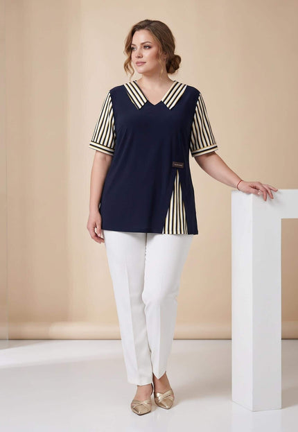 Ολόσωμη λήψη με κομψή γυναικεία τουνίκ plus size σε σκούρο μπλε χρώμα με ριγέ λεπτομέρειες, συνδυασμένη με λευκό παντελόνι.