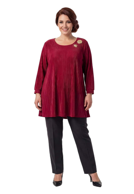 Ολόσωμη λήψη: Κομψή επίσημη κόκκινη τουνίκ σε μεγάλα μεγέθη, με πλισέ υφή, μανίκια 7/8 και εντυπωσιακές χρυσές καρφίτσες, σε λευκό φόντο.