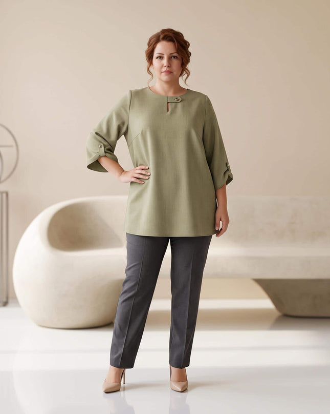 Ολόσωμη λήψη με γυναίκα plus size που φοράει κομψή επίσημη τουνίκ σε λαδί χρώμα με μανίκια 3/4, συνδυασμένη με γκρι παντελόνι.