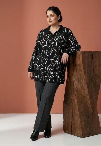 Κομψή γυναικεία τουνίκ plus size με λευκό αφηρημένο print και μαύρο γιακά, σε ολόσωμη λήψη με το μοντέλο να ποζάρει δίπλα σε ξύλινο βάθρο.