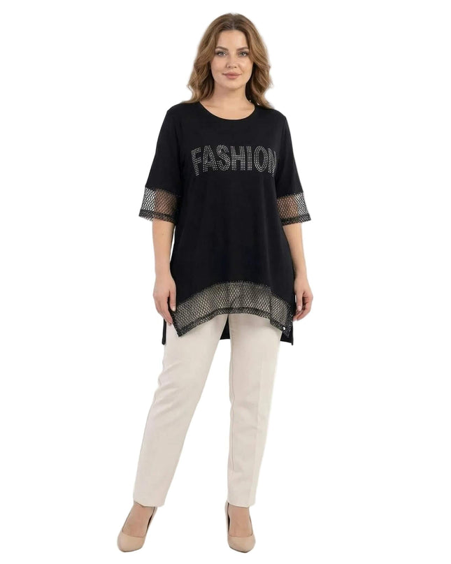 Ολόσωμη λήψη. Μαύρη ασύμμετρη τουνίκ plus size με λεπτομέρειες από δίχτυ και στρας που σχηματίζουν τη λέξη FASHION, φορεμένη με ανοιχτόχρωμο παντελόνι.