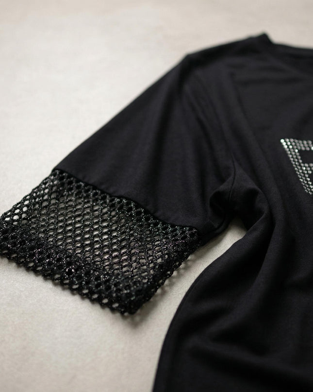 Κοντινή λεπτομέρεια από τη μαύρη τουνίκ σε μεγάλα μεγέθη, που αναδεικνύει το μανίκι με το λαμπερό δίχτυ και την αστραφτερή επιγραφή από στρας.