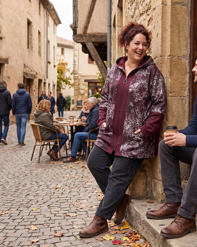 Γυναίκα που φοράει plus size μπορντό ζακέτα με κουκούλα και σχέδια, σε ολόσωμη λήψη σε πέτρινο σοκάκι.