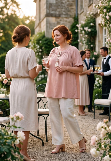 Ολόσωμη λήψη με κομψή ροζ γυναικεία τουνίκ plus size, που διαθέτει κορδόνια στη λαιμόκοψη, σε μια κομψή κοινωνική εκδήλωση σε κήπο.