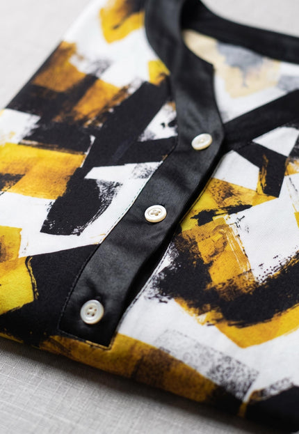 Κοντινή λεπτομέρεια από γυναικείο εμπριμέ πουκάμισο σε μεγάλα μεγέθη, με μοντέρνο κίτρινο-μαύρο σχέδιο, μαύρη πατιλέτα και λευκά κουμπιά.