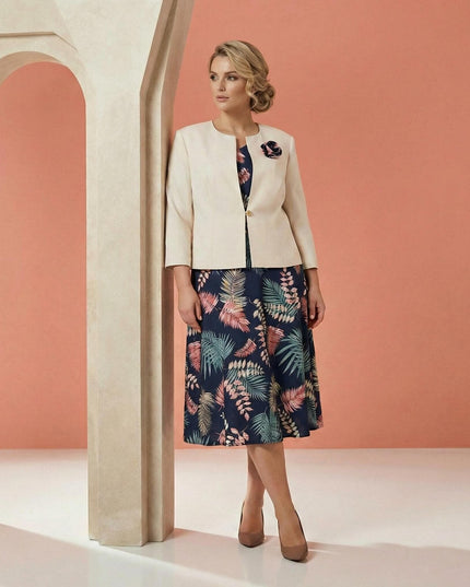 Κομψό γυναικείο ταγιέρ σε μεγάλα μεγέθη που αποτελείται από μπλε φλοράλ φόρεμα και μπεζ σακάκι με διακοσμητικό λουλούδι, σε ολόσωμη λήψη.