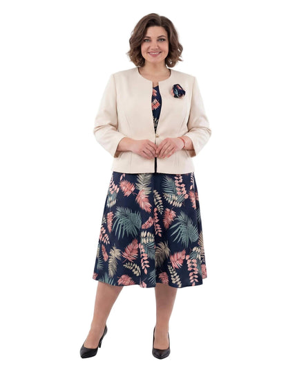 Κομψό γυναικείο ταγιέρ σε μεγάλα μεγέθη που περιλαμβάνει μπλε φλοράλ φόρεμα και μπεζ σακάκι με διακοσμητικό λουλούδι, σε ολόσωμη λήψη.