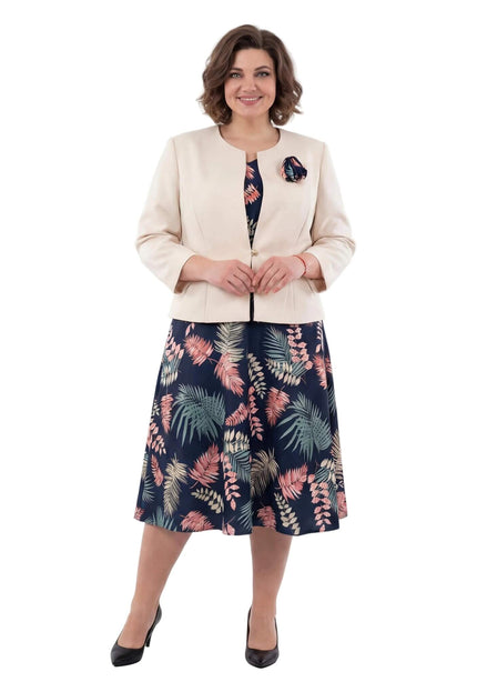 Κομψό γυναικείο ταγιέρ σε μεγάλα μεγέθη που περιλαμβάνει μπλε φλοράλ φόρεμα και μπεζ σακάκι με διακοσμητικό λουλούδι, σε ολόσωμη λήψη.