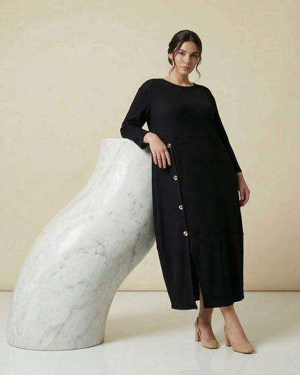 Ολόσωμη λήψη: Κομψό μαύρο επίσημο εβαζέ φόρεμα σε μεγάλα μεγέθη, με ριμπ ύφανση, 7/8 μανίκια και διακοσμητικά χρυσά κουμπιά στο πλάι.