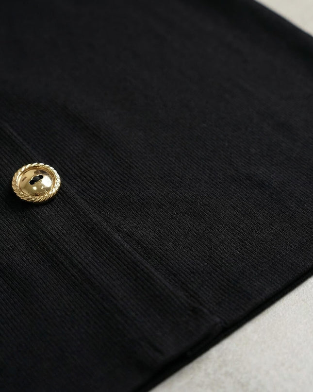 Κοντινή λεπτομέρεια από το μαύρο ριμπ ύφασμα του επίσημου φορέματος σε μεγάλα μεγέθη, με εστίαση στο εντυπωσιακό χρυσό διακοσμητικό κουμπί.