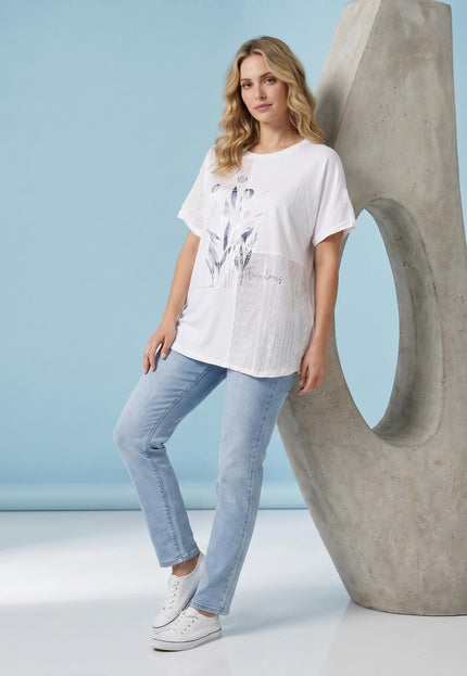 Ολόσωμη λήψη μοντέλου με λευκή καλοκαιρινή τουνίκ plus size, που διαθέτει φλοράλ απλικέ και κοντά μανίκια, σε γαλάζιο φόντο.