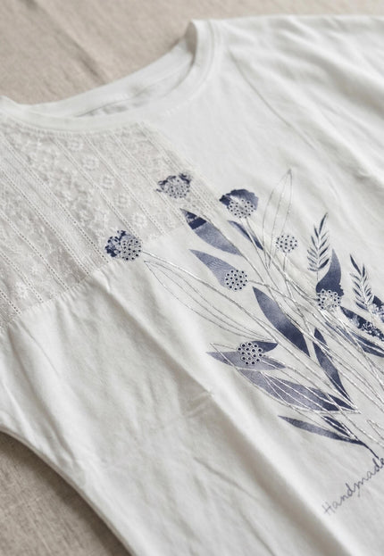 Κοντινή λεπτομέρεια σε flat lay από λευκή καλοκαιρινή τουνίκ plus size. Αναδεικνύεται το μπλε φλοράλ σχέδιο και η διακριτική δαντέλα στον ώμο.