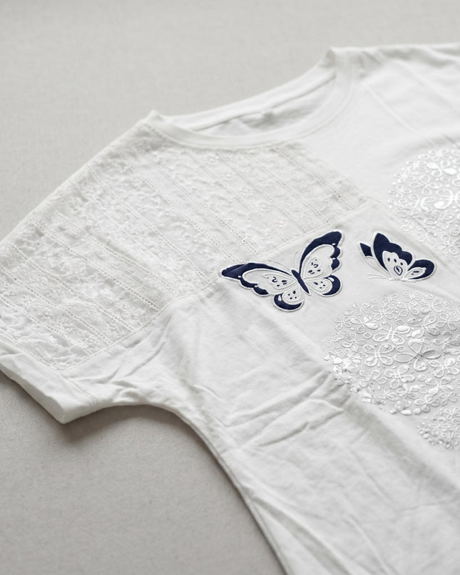 Κοντινή λεπτομέρεια σε λευκή βαμβακερή τουνίκ plus size, όπου διακρίνονται η κομψή δαντέλα στο μανίκι και το εντυπωσιακό απλικέ με σκούρες μπλε πεταλούδες.