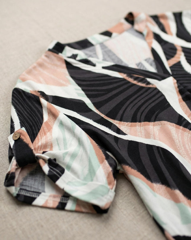 Κοντινή λεπτομέρεια του μανικιού με κουμπί και του πολύχρωμου μοτίβου σε καλοκαιρινή τουνίκ plus size, τραβηγμένη σε flat lay.